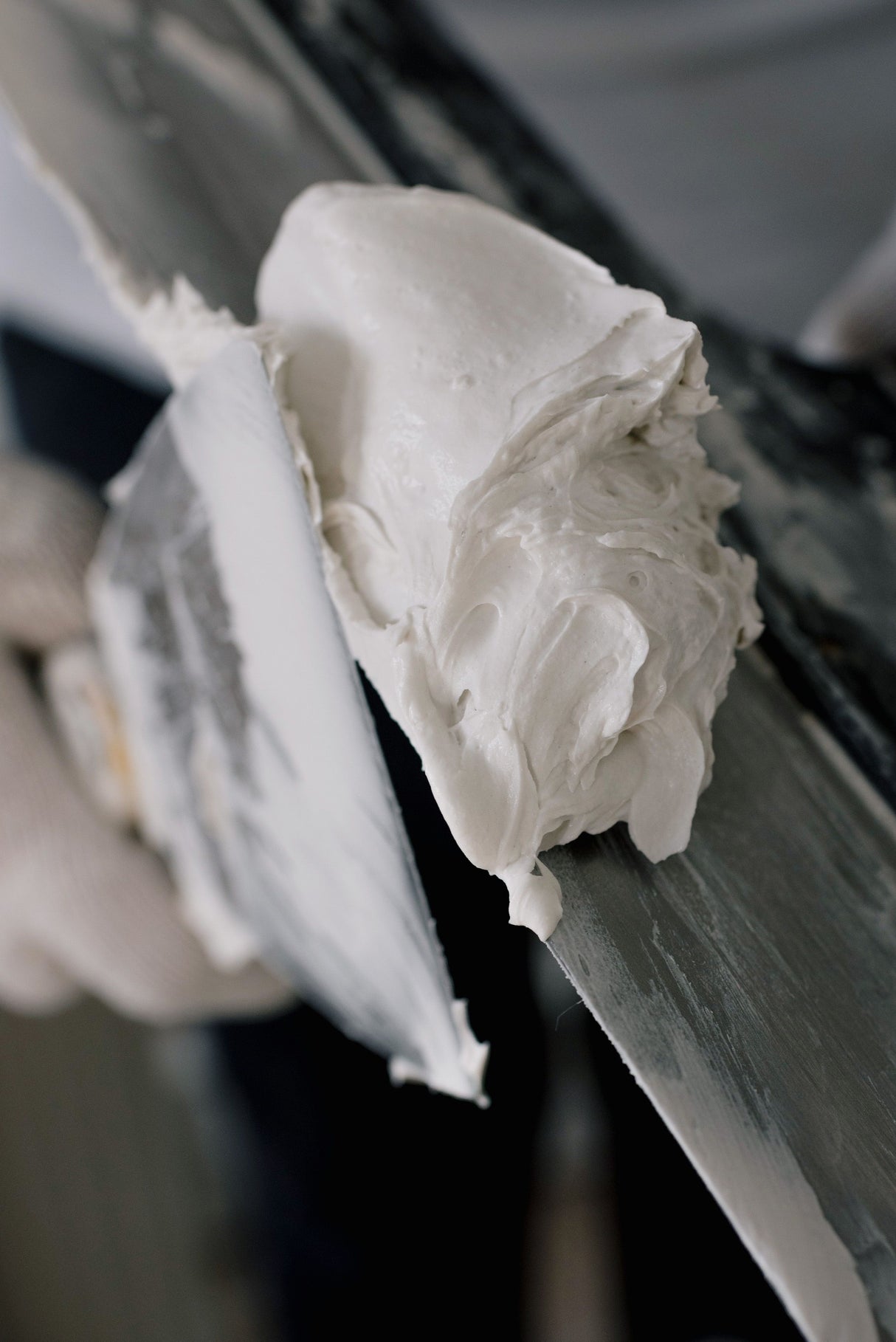 Close up of a hand holding a metal filling knife covered in spackle