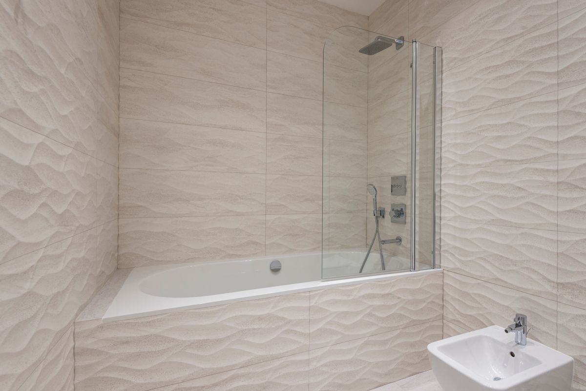 Sleek modern bathroom with beige textured tiles and bathtub, complementing Dulux Egyptian Cotton