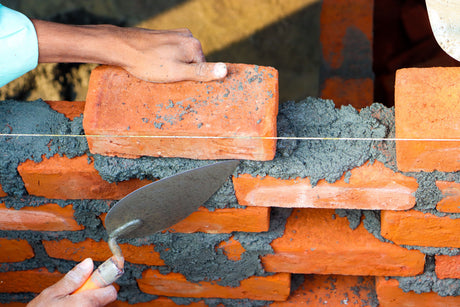 Hands using a trowel to work jointing compound firmly into a paving joint
