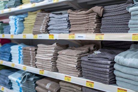 Rows of folded tea towels in different colours and patterns displayed together on a shop shelf
