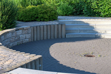 Wide view of a modern circular stone patio with paving joints surrounded by neat garden landscaping