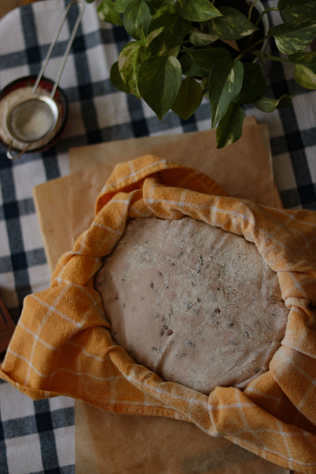 Ball of bread dough resting in a bowl and covered with a folded cotton tea towel to rise