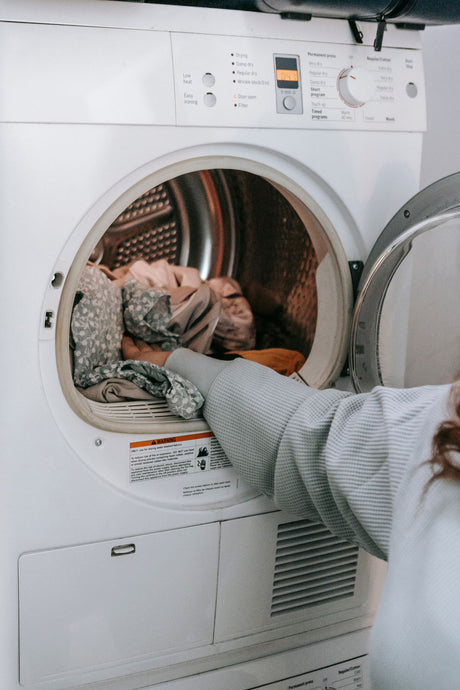 Woman loading a mixed load of laundry into an open front-loading washing machine at home