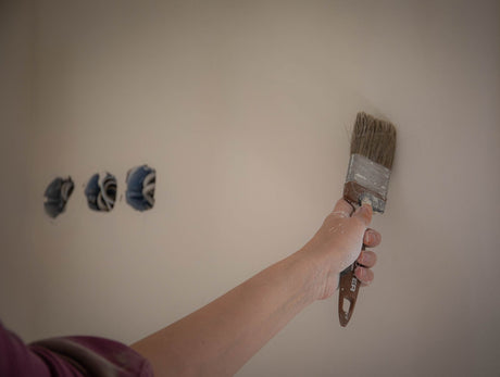 Decorator using a paint brush to cut in paint around a wall during a home renovation