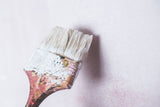 Painter applying masonry paint to an exterior wall with a brush