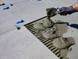 Gloved hand brushing jointing compound firmly into the gaps between outdoor paving slabs