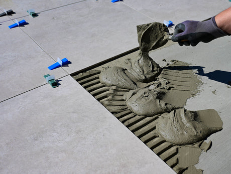 Gloved hand brushing jointing compound firmly into the gaps between outdoor paving slabs