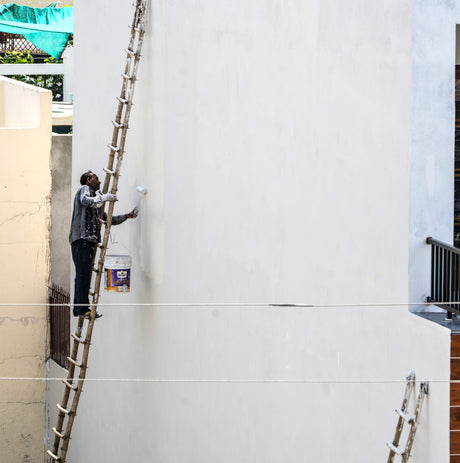 Worker on a ladder applying masonry paint to an exterior building wall