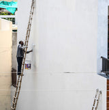 Worker on a ladder applying masonry paint to an exterior building wall