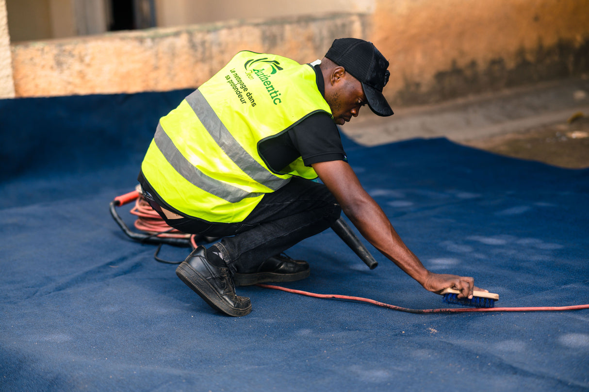 Worker using a brush to work carpet cleaning foam into a soiled carpet