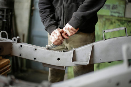 Person using a wire brush to scrub rust from a metal surface before painting