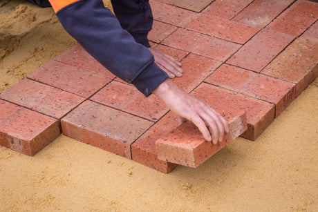 Worker bedding a paving slab in place during patio installation, before jointing