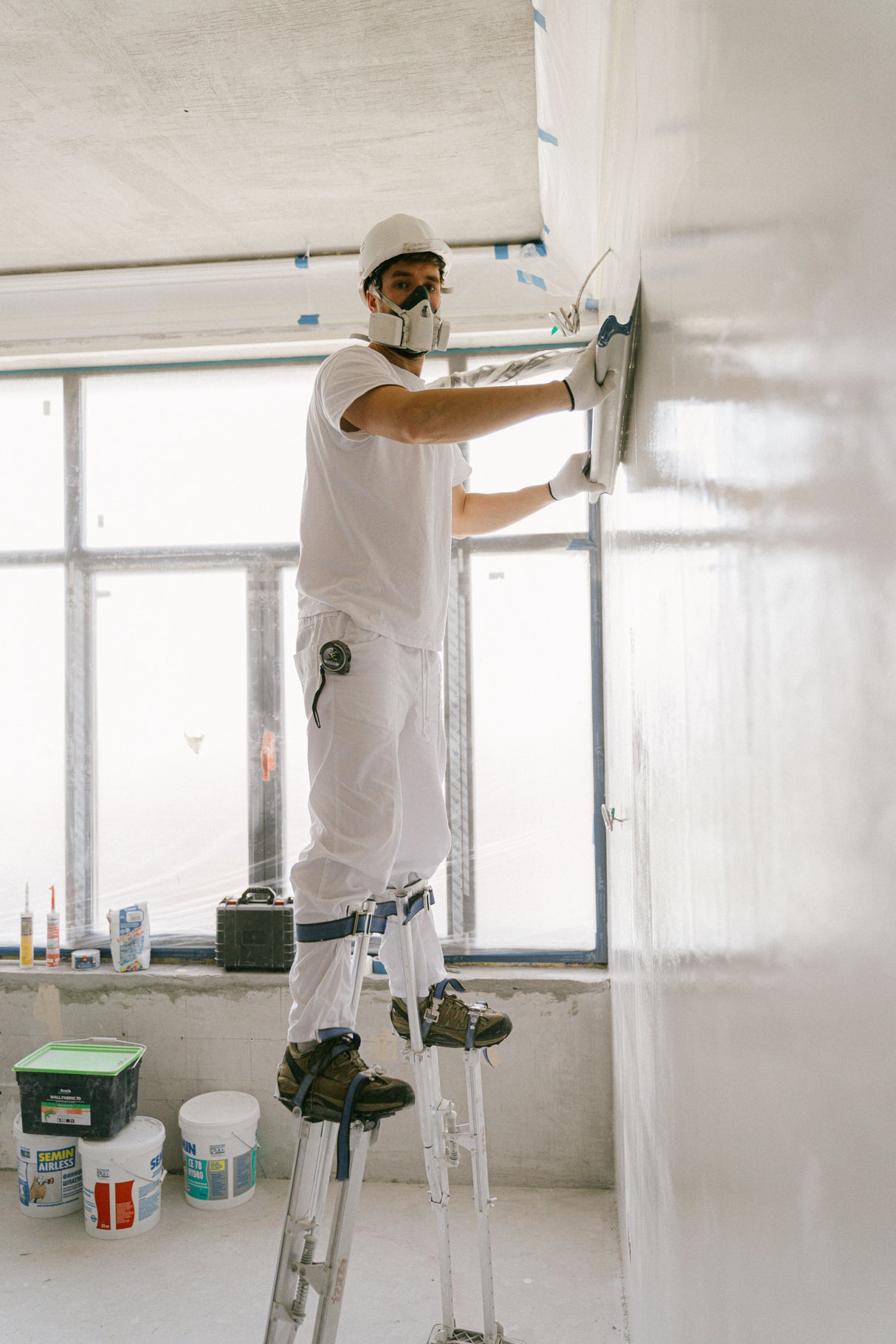 Worker smoothing joint compound into a corner while wearing safety gear