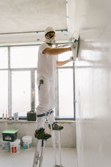 Worker smoothing joint compound into a corner while wearing safety gear