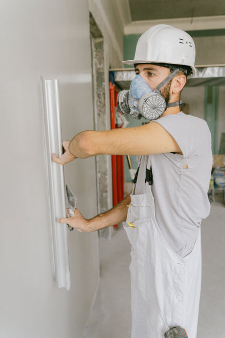 Construction worker smoothing a large section of wall with a wide blade knife