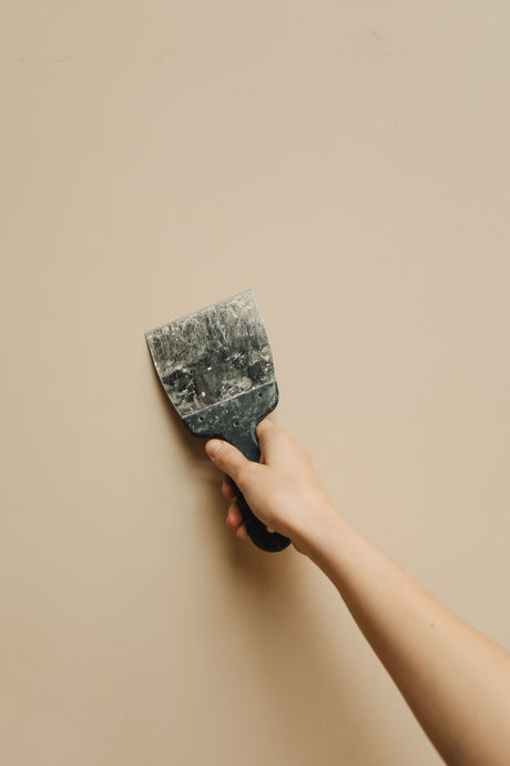 Close up of a hand holding a flexible joint knife blade against a wall