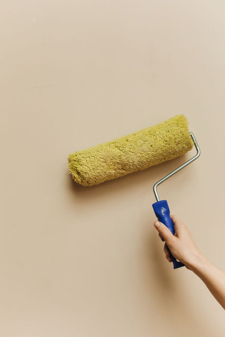 Hand using a paint roller to apply a fresh coat on a beige wall, application technique for Dulux Quick Dry Satinwood