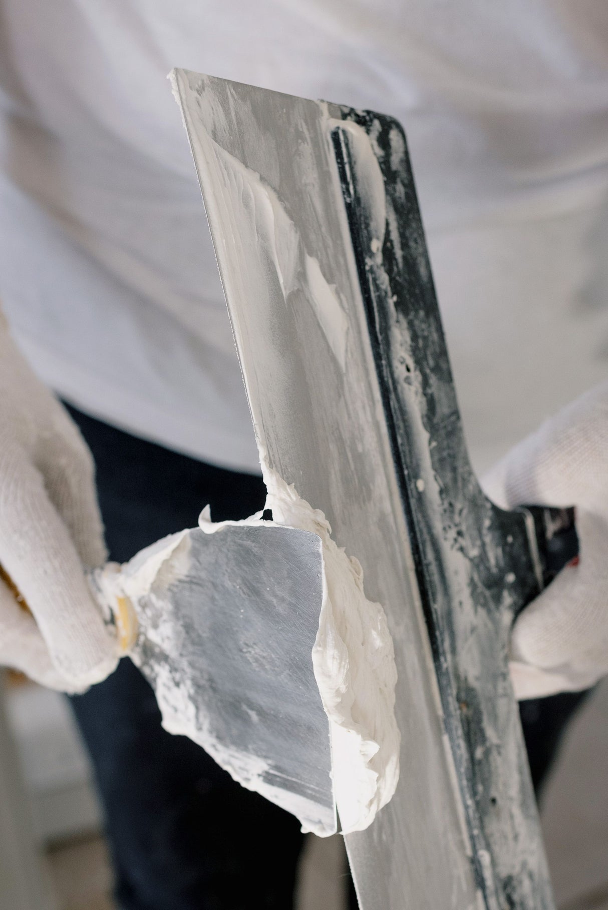 Decorator in gloves holding a wide filling knife while working on plasterboard