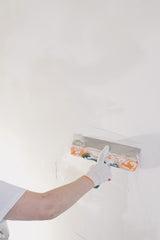Decorator in gloves using a filling knife to plaster an internal wall corner