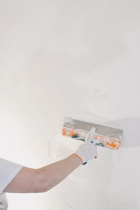 Decorator in gloves using a filling knife to plaster an internal wall corner