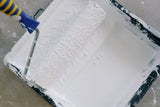 Paint roller loaded with masonry paint in a roller tray ready to apply