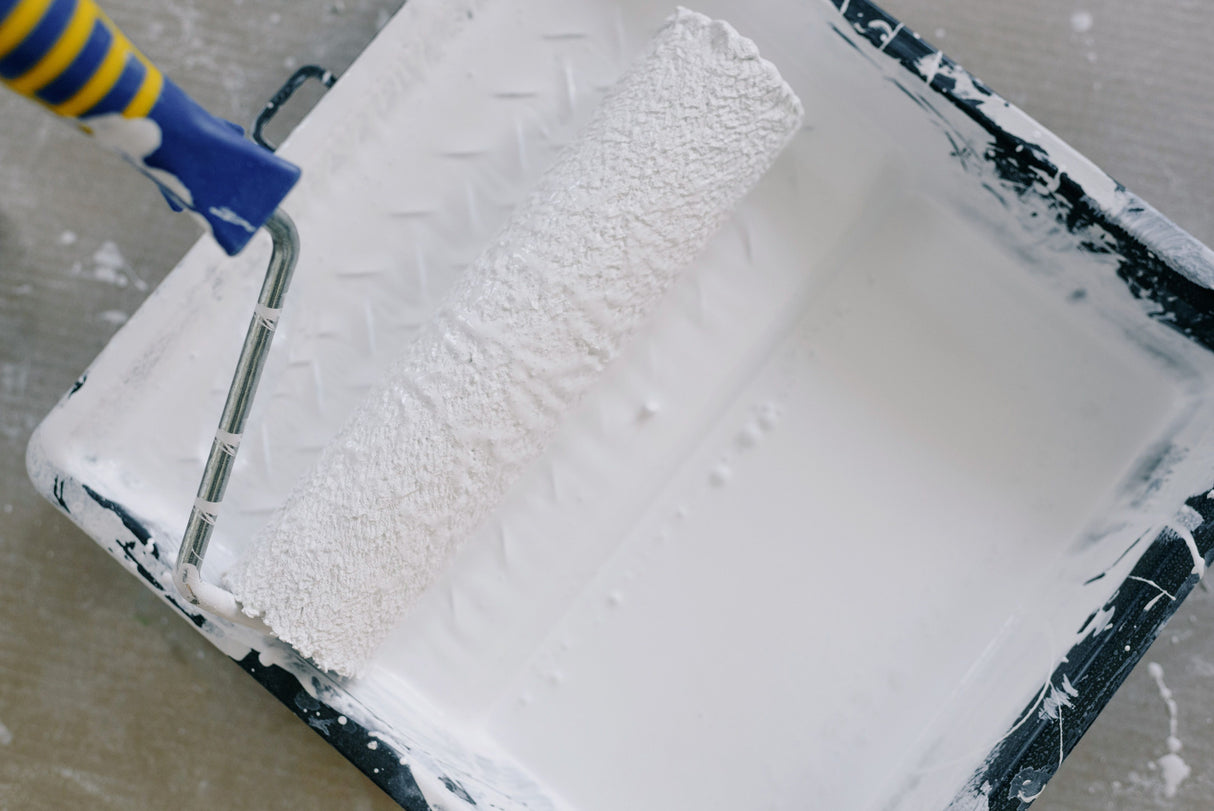 Paint roller loaded with masonry paint in a roller tray ready to apply