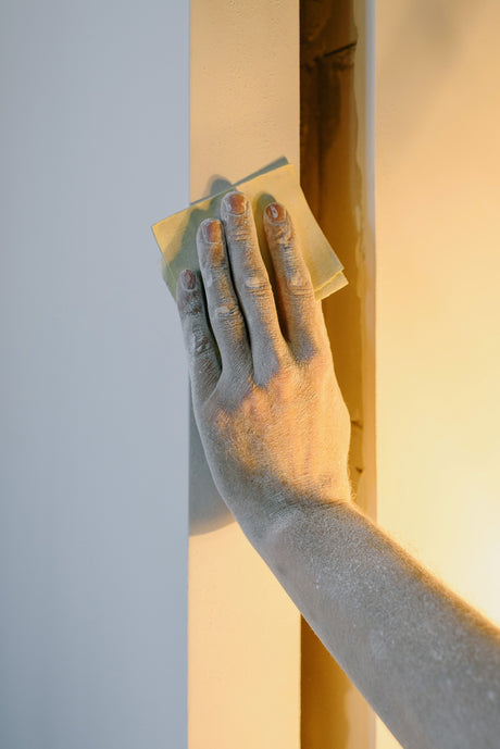 Person preparing a wall surface with a hand tool before painting