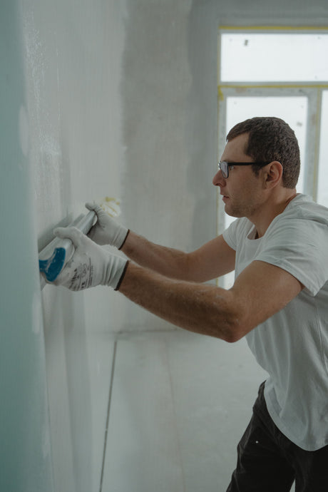 Worker applying drywall joint compound to a plasterboard seam indoors