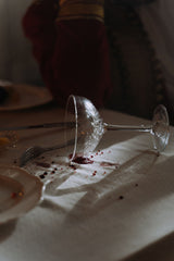 Overturned wine glass with a fresh red wine stain spreading across pale fabric