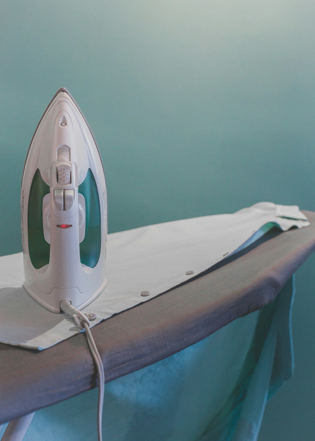 Steam iron plugged in and resting on an ironing board, demonstrating typical everyday use of an ironing board cover