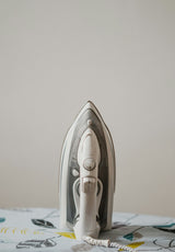 White and grey steam iron resting on an ironing board, demonstrating typical everyday use of an ironing board cover