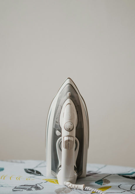 White and grey steam iron resting on an ironing board, demonstrating typical everyday use of an ironing board cover