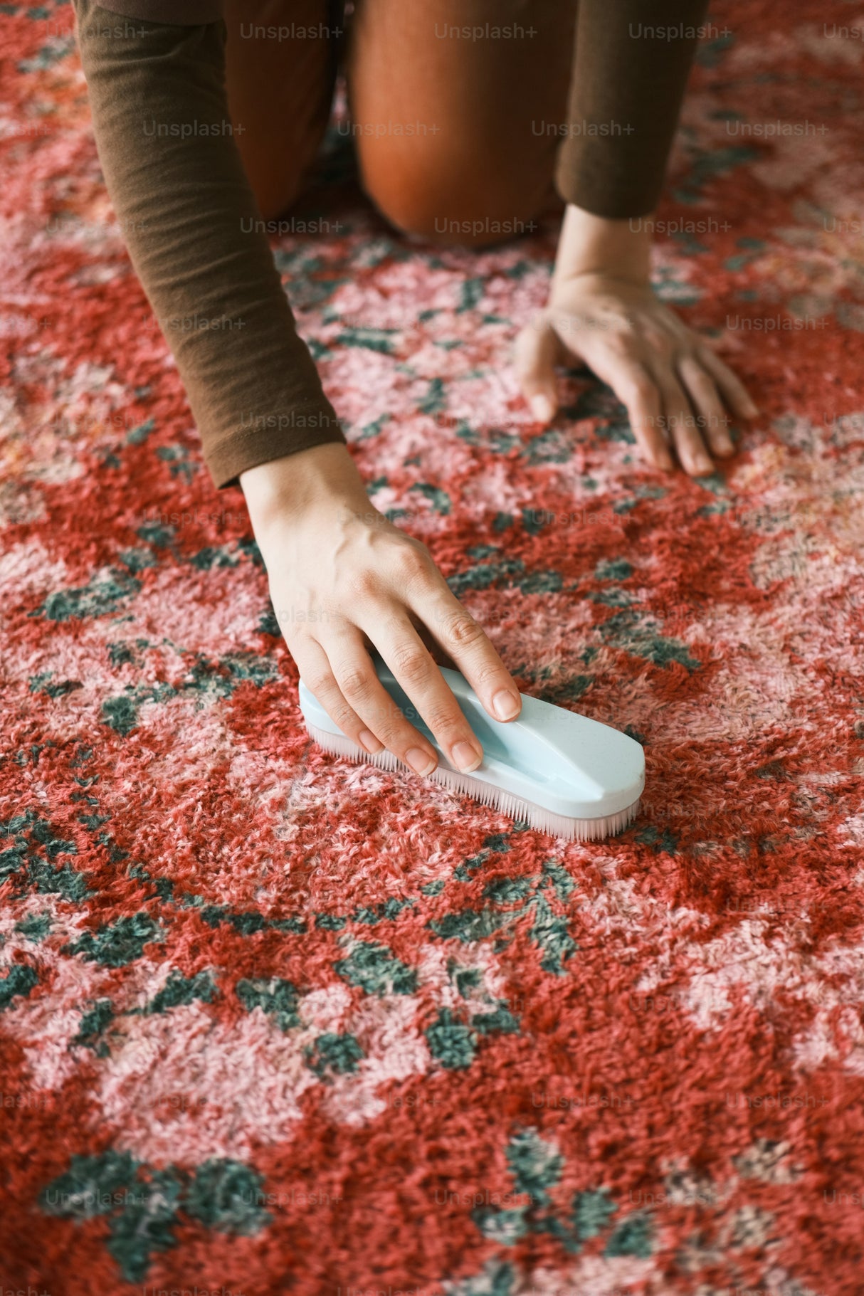 Person kneeling on a rug and working a stain into the fibres with a cleaning brush