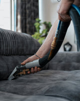 Hands cleaning and scrubbing fabric upholstery on a sofa